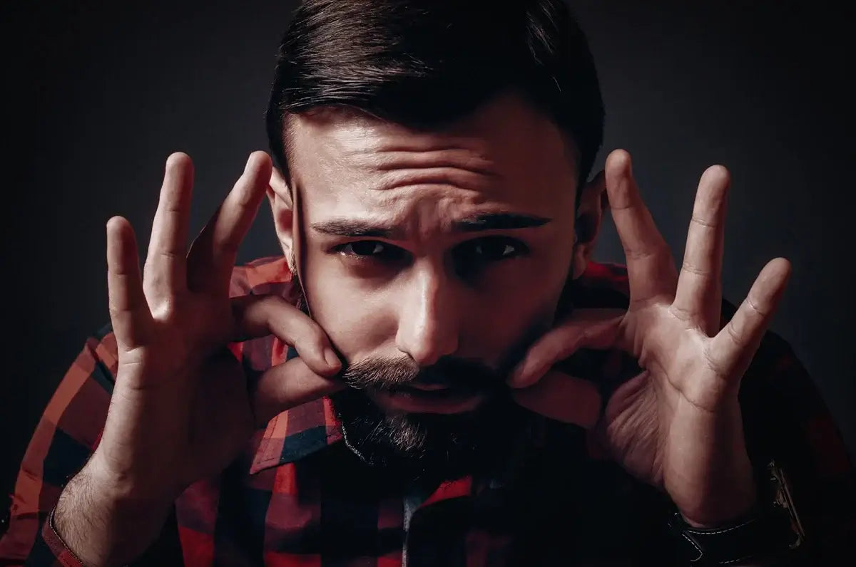 Man in red flannel shirt shaping mustache with fingers while looking intensely at camera