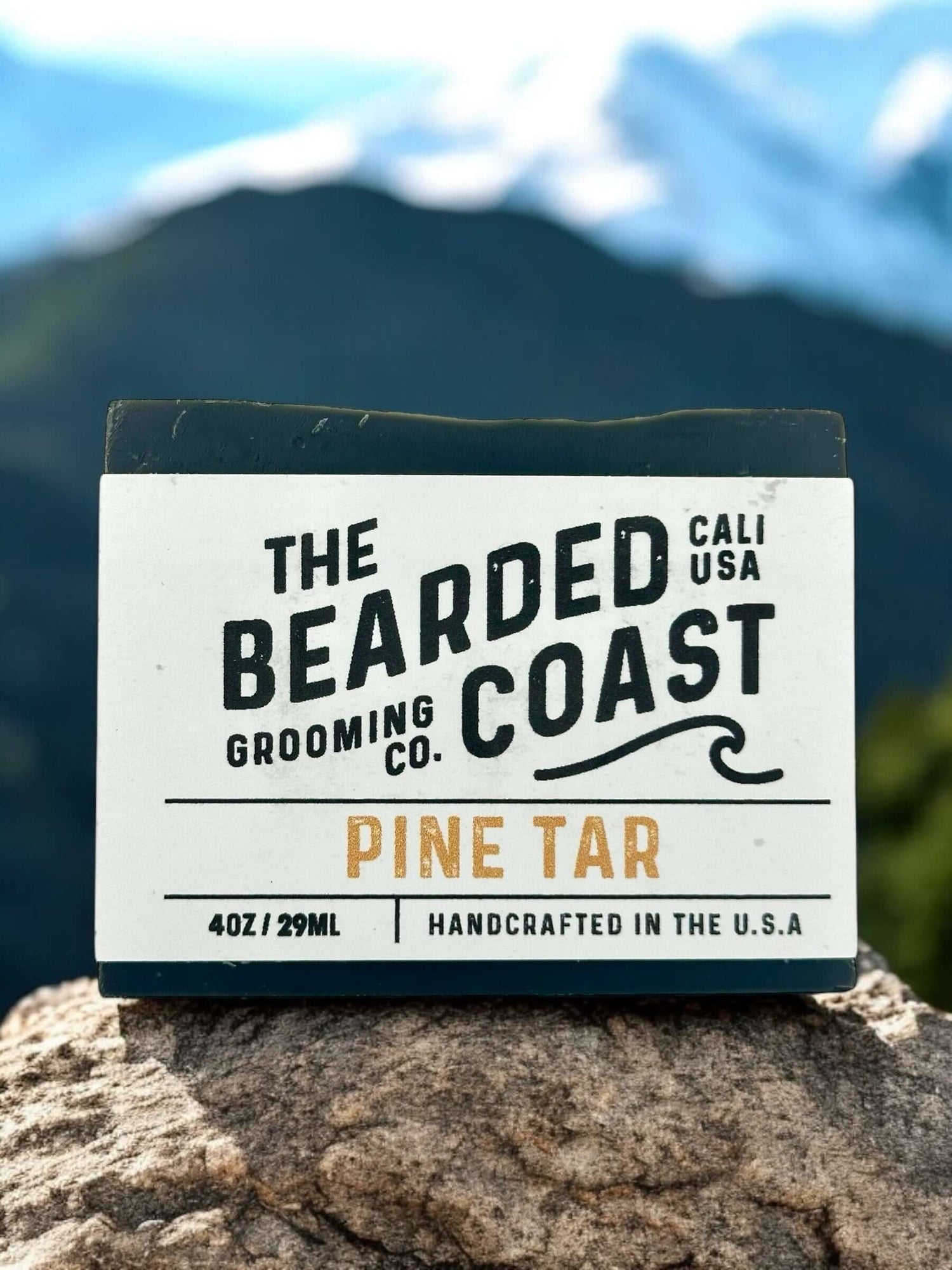 Pine tar soap from Bearded Coast, handcrafted in the USA, displayed on a rocky surface with mountains in background.