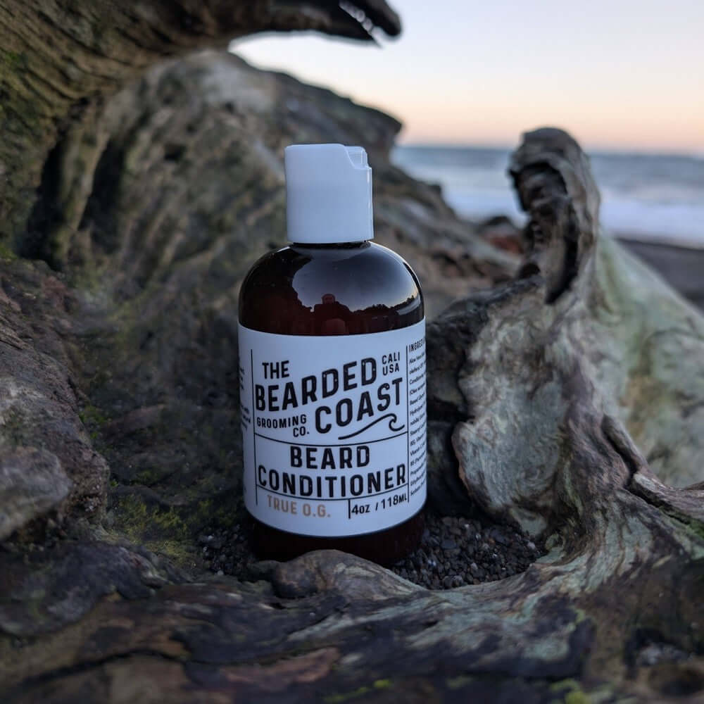 The Bearded Coast beard conditioner bottle on a natural wood background near the beach.