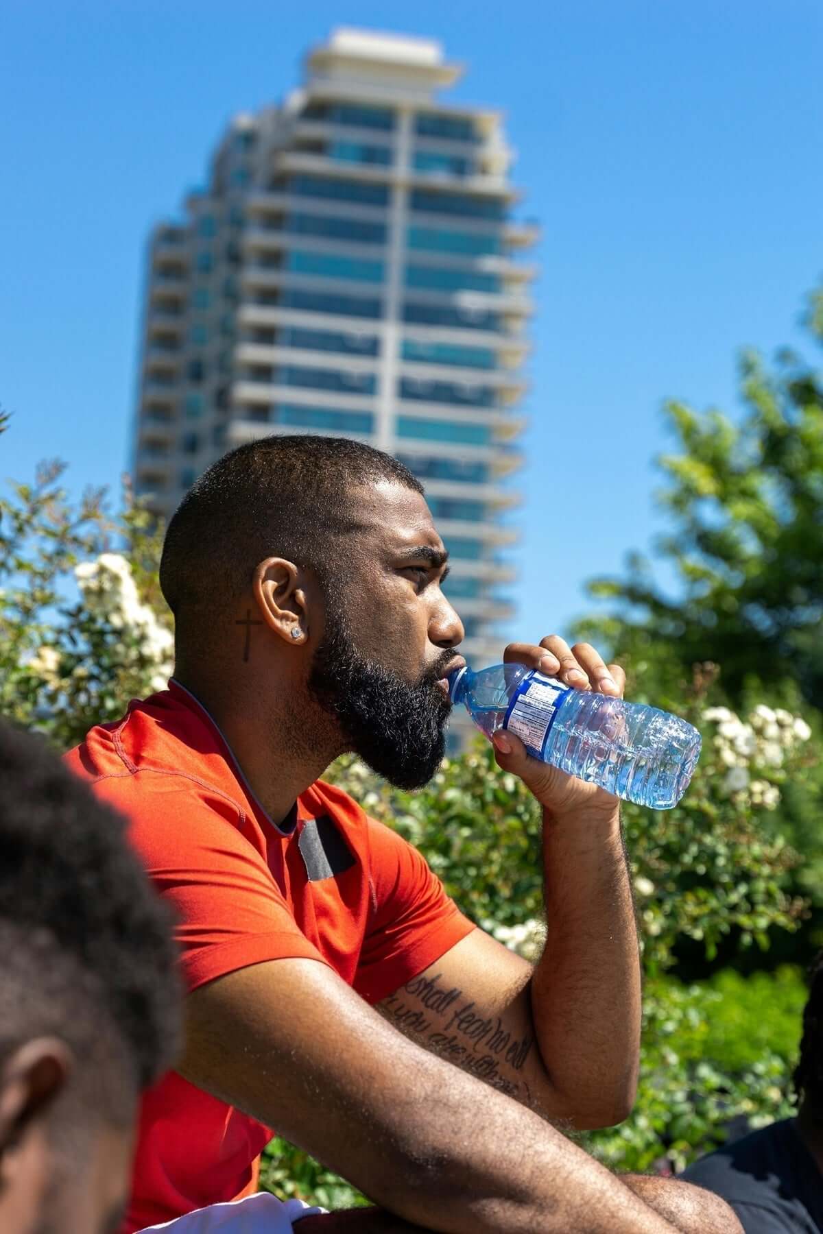 Man with a beard drinking water outdoors, emphasizing hydration for beard and skin health.