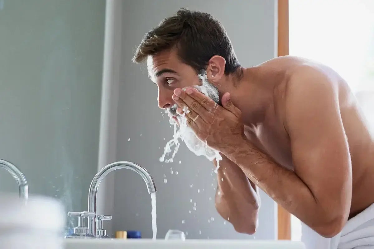 Man rinsing beard at bathroom sink with foaming cleanser and running water
