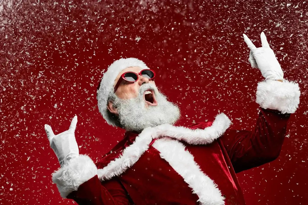 Rock ‘n’ roll Santa in red velvet suit and sunglasses throwing horns amid falling snow.