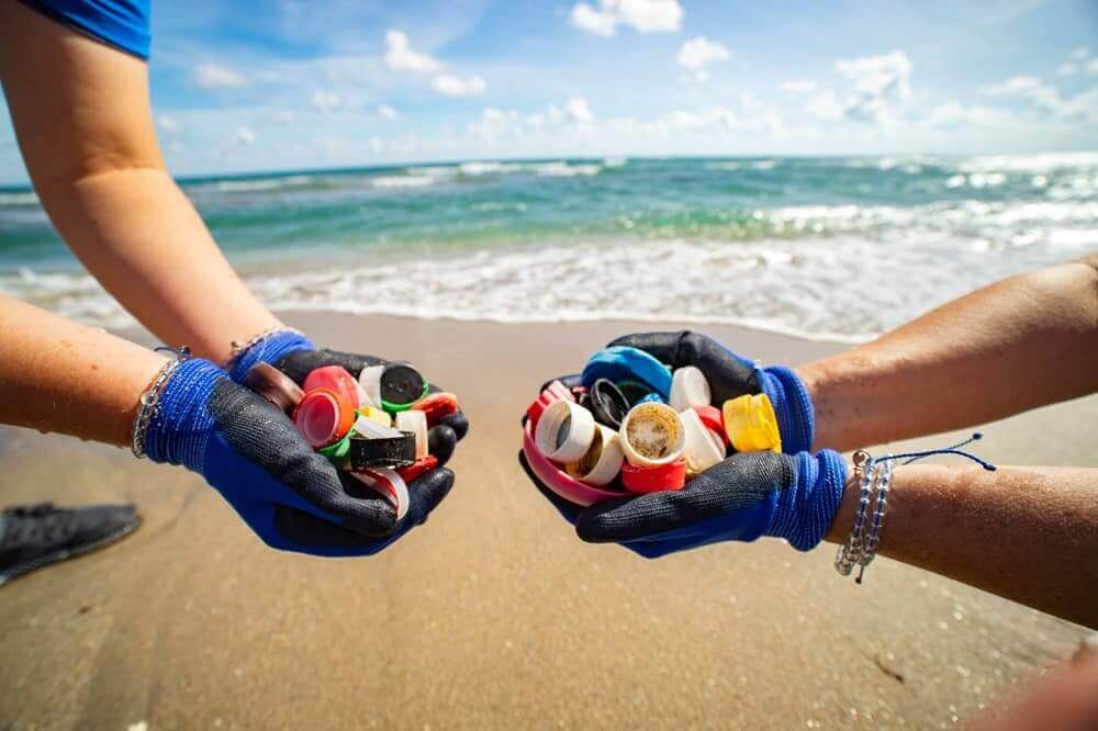 Two pairs of hands holding plastic debris collected from the beach, symbolizing ocean cleanup efforts.