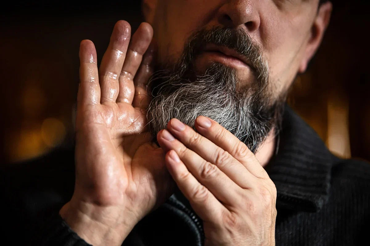 person applying beard oil to grey beard with hands pressing through to skin