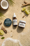 Bearded Coast Beard care products including balm, oil, and butter on a sandy surface with coconut and lime elements.