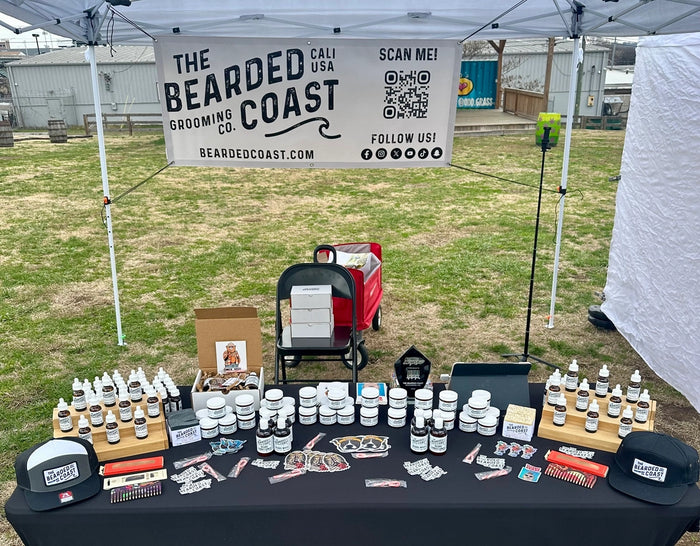 Bearded Coast grooming products displayed on a table under a branded tent.