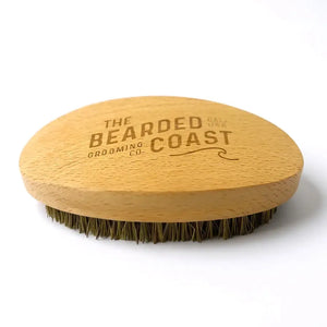 Curved wooden vegan beard brush with natural bristles and Bearded Coast logo engraved on the handle.