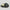 Open dark charcoal metal tin of The Bearded Coast Grooming Co. Old Skool Premium Natural Beard Balm, 2 oz / 57g, lid leaning against the base showing smooth pale yellow balm texture, on a light gray background