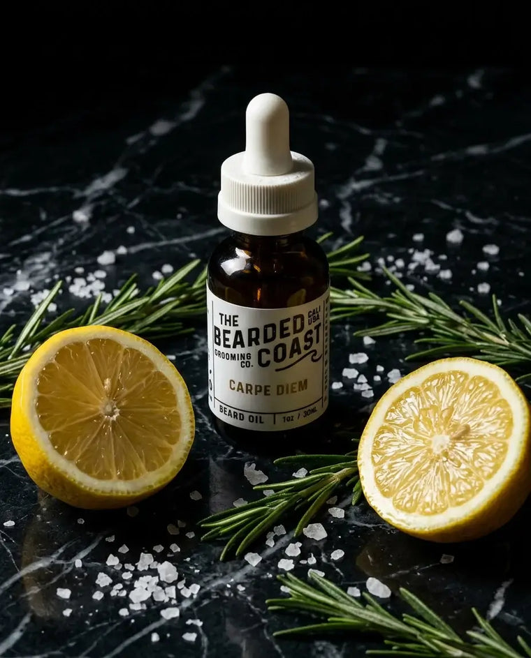 Amber dropper bottle of Bearded Coast Grooming Co. Carpe Diem Beard Oil, 1oz/30ml, surrounded by fresh lemon halves, rosemary sprigs, and sea salt flakes on a dark black marble surface.