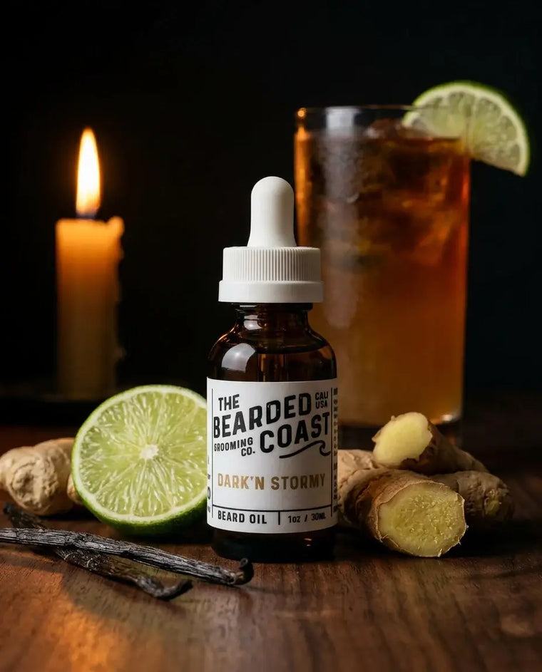 Amber dropper bottle of Bearded Coast Grooming Co. Dark'N Stormy Beard Oil, 1oz/30ml, on a dark wood table surrounded by fresh lime, raw ginger root, and vanilla beans, with a dark rum and ginger beer cocktail and a lit candle glowing in the background.