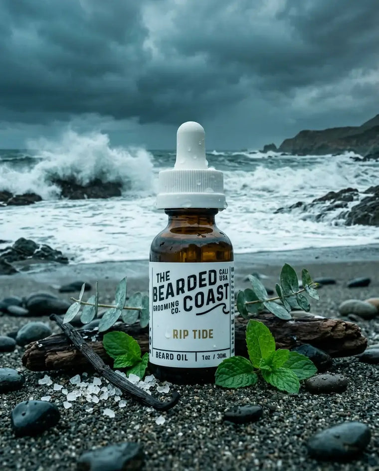 Amber dropper bottle of Bearded Coast Grooming Co. Rip Tide Beard Oil, 1oz/30ml, standing on a rocky shoreline surrounded by fresh mint leaves, eucalyptus sprigs, vanilla beans, and sea salt crystals, with dramatic crashing waves and a stormy sky in the background.