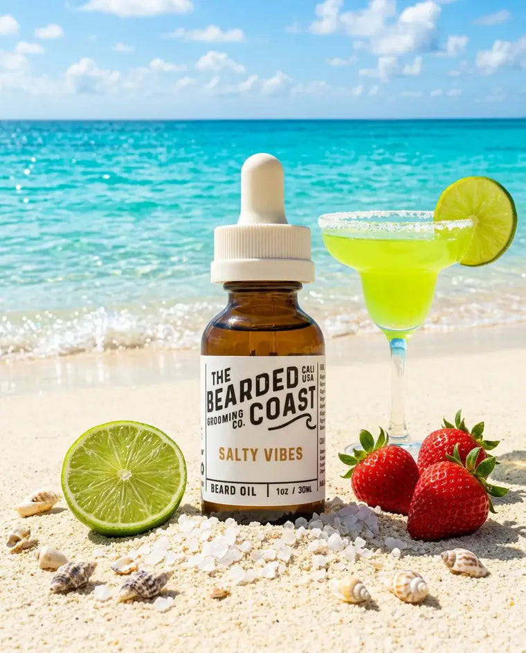 Amber dropper bottle of Bearded Coast Grooming Co. Salty Vibes Beard Oil, 1oz/30ml, standing on a sunny white sand beach surrounded by fresh lime, strawberries, sea salt crystals, and seashells, with a salted-rim margarita and turquoise ocean in the background.