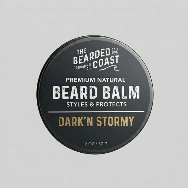 Top-down view of The Bearded Coast Grooming Co. Dark'n Stormy Premium Natural Beard Balm — a 2 oz / 57g dark charcoal metal tin with gold and white typography on a gray background