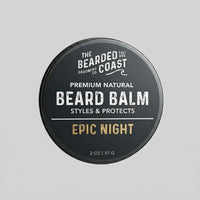 Top-down view of The Bearded Coast Grooming Co. Epic Night Premium Natural Beard Balm — a 2 oz / 57g dark charcoal metal tin with gold and white typography on a gray background