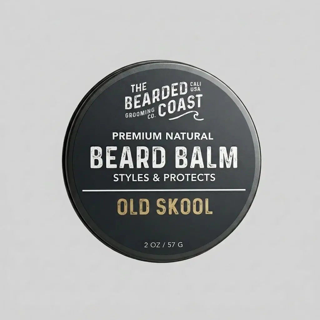 Top-down view of The Bearded Coast Grooming Co. Old Skool Premium Natural Beard Balm — a 2 oz / 57g dark charcoal metal tin with gold and white typography on a gray background