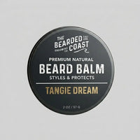 Top-down view of The Bearded Coast Grooming Co. Tangie Dream Premium Natural Beard Balm — a 2 oz / 57g dark charcoal metal tin with gold and white typography on a gray background