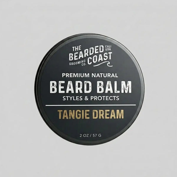 Top-down view of The Bearded Coast Grooming Co. Tangie Dream Premium Natural Beard Balm — a 2 oz / 57g dark charcoal metal tin with gold and white typography on a gray background