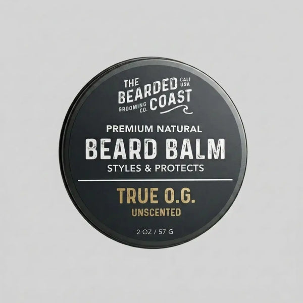 Top-down view of The Bearded Coast Grooming Co. True O.G. Premium Natural Beard Balm — a 2 oz / 57g dark charcoal metal tin with gold and white typography on a gray background